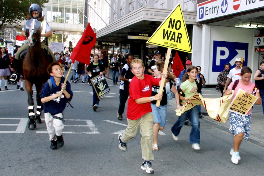 School children run through a city street holding No War signs with mounted police behind them