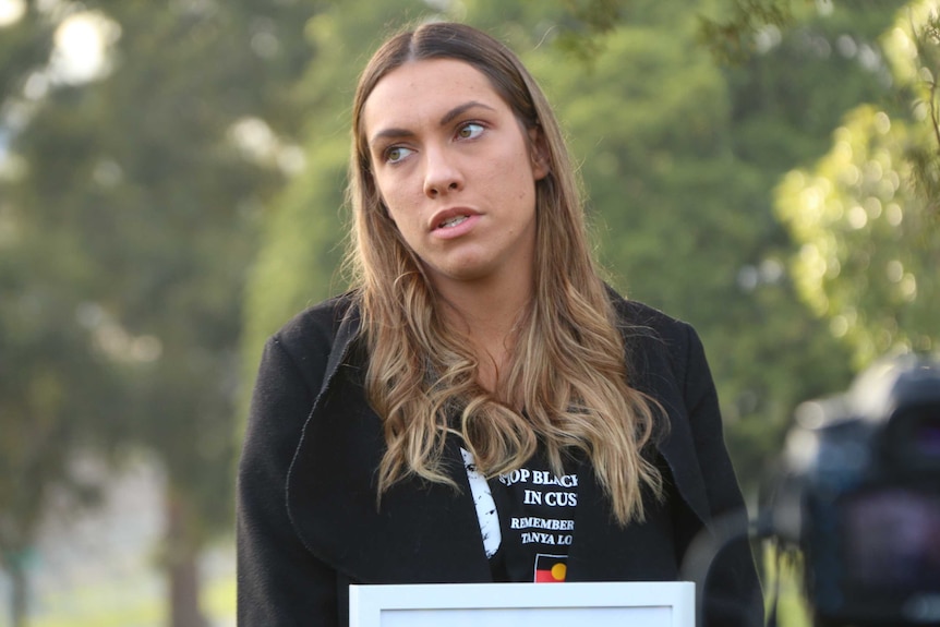 Apryl Watson stands holding a framed photo of her mother, Tanya Day, in a Melbourne garden.