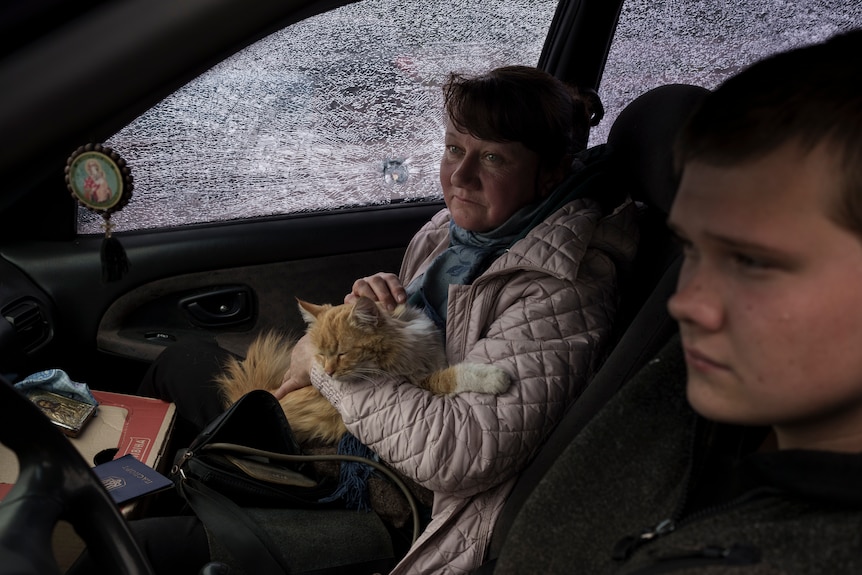 A woman seated in a car with her cat and her son sitting beside her.