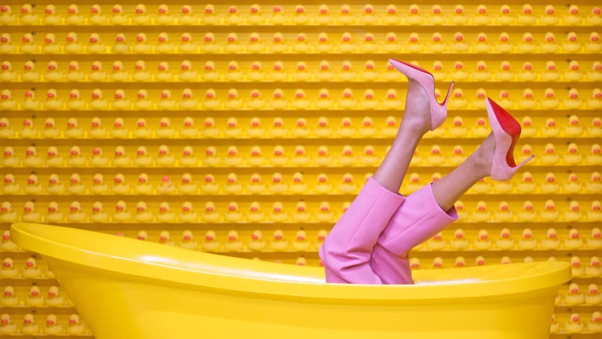 A pair of trousered woman's legs wearing pink heels emerging from yellow bathtub