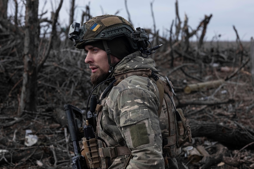 An Ukrainian soldier stands amongsy a burnst forest 