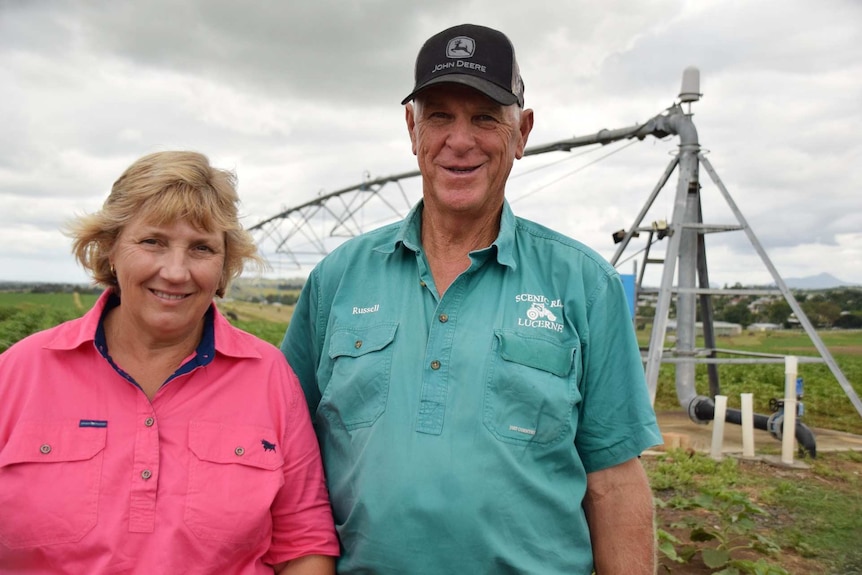 Two farmers smile in a paddock.