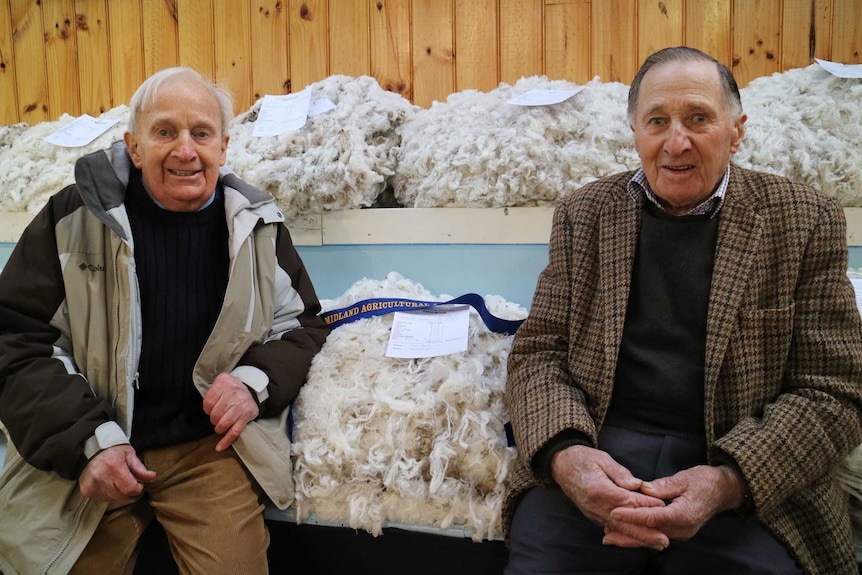 two men sit next to piles of superfine wool