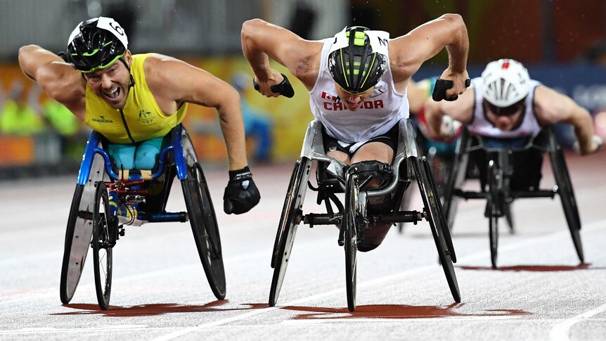 Two men in racing wheelchairs cross the finish line on an athletics track.