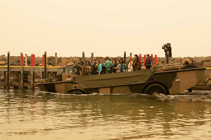 About 30 people are seen aboard a LARC by a dock. The sky above is hazy.