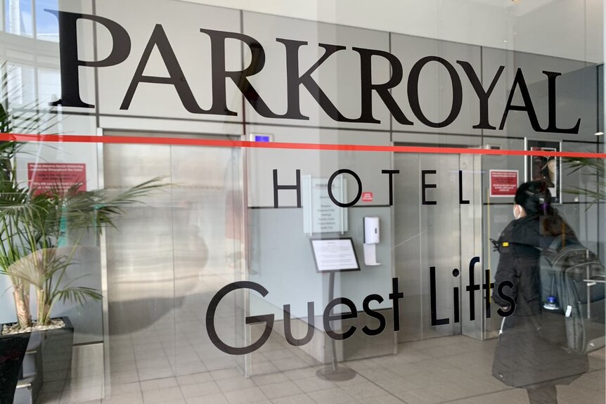 A hotel lobby with a woman waiting for a lift and signage saying Parkroyal Hotel.