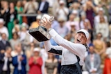 A woman lifts a tennis trophy in triumph.