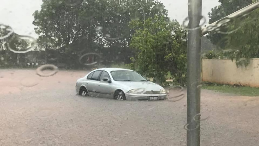 A car sits stranded in muddy floodwaters on the side of a road in Broome.