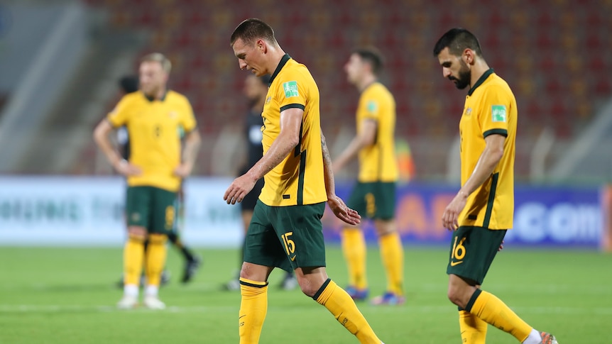 Australia players look sad as they walk sideways on a soccer field