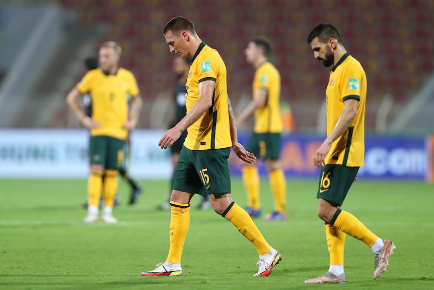 Australia players look sad as they walk sideways on a soccer field