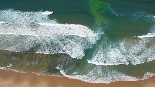 A greeny blue channel between white capped waves breaking into the shore. 