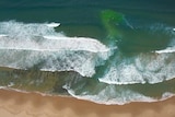 A greeny blue channel between white capped waves breaking into the shore. 
