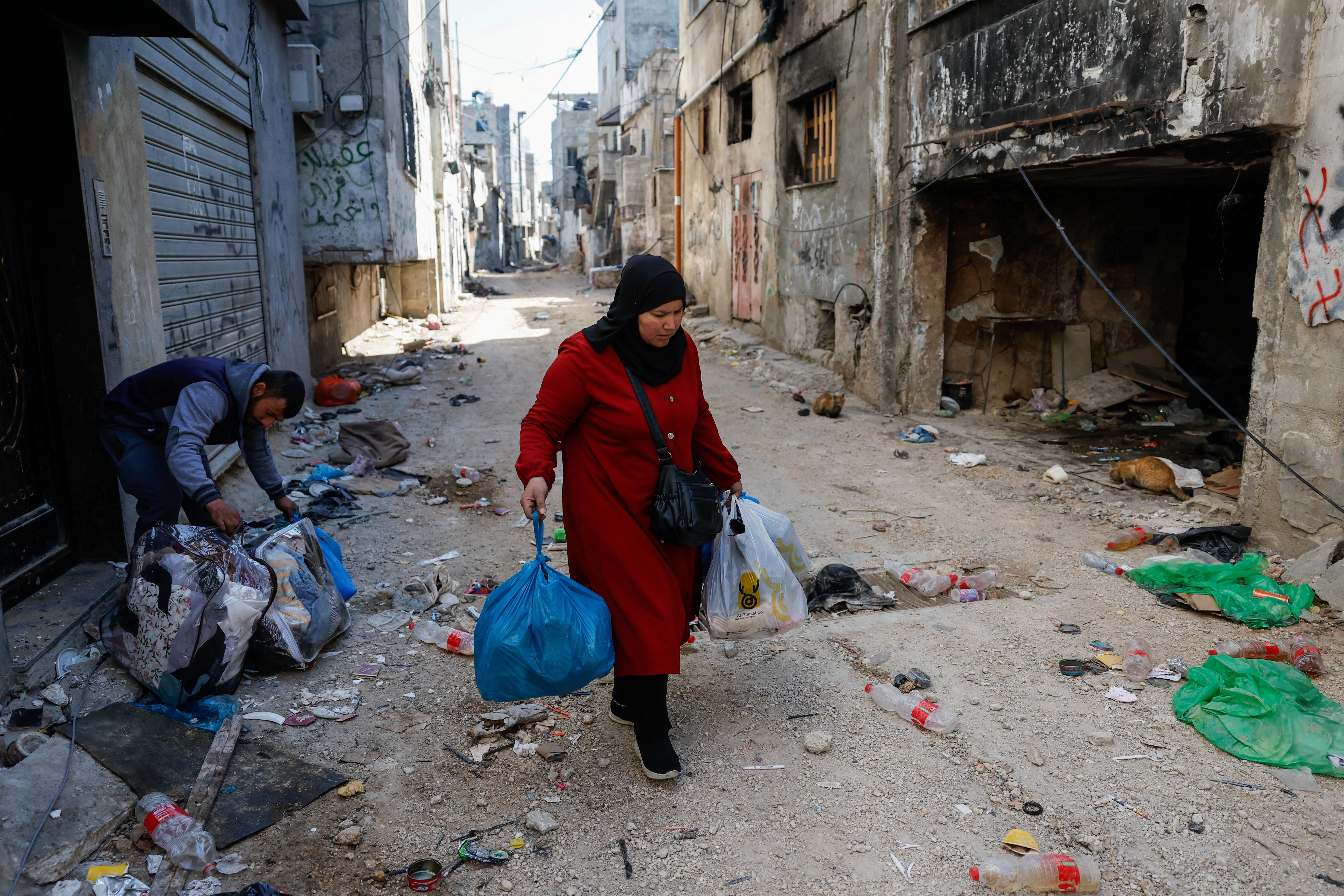 A Palestinian woman walks with her belongings along a dirt path.