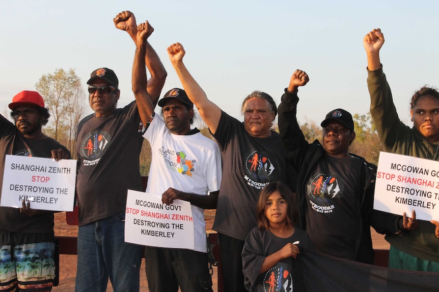 A number of protesters with their arms in the air standing at gate to cattle station