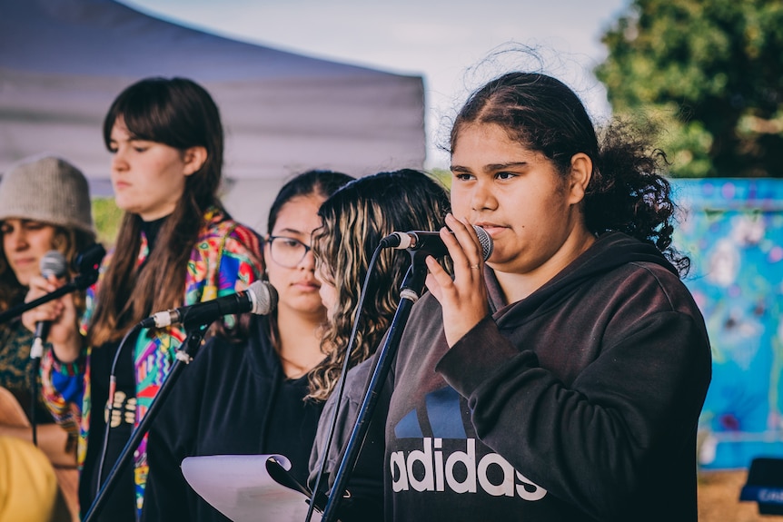 An Indigenous student and singer stands at a microphone.