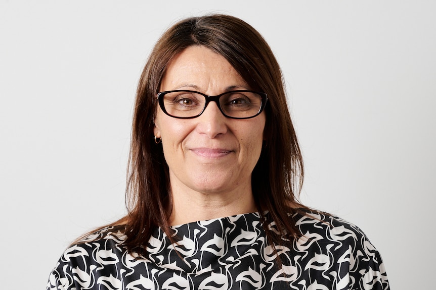 A woman in glasses with brown hair and a black and white top looks at the camera 