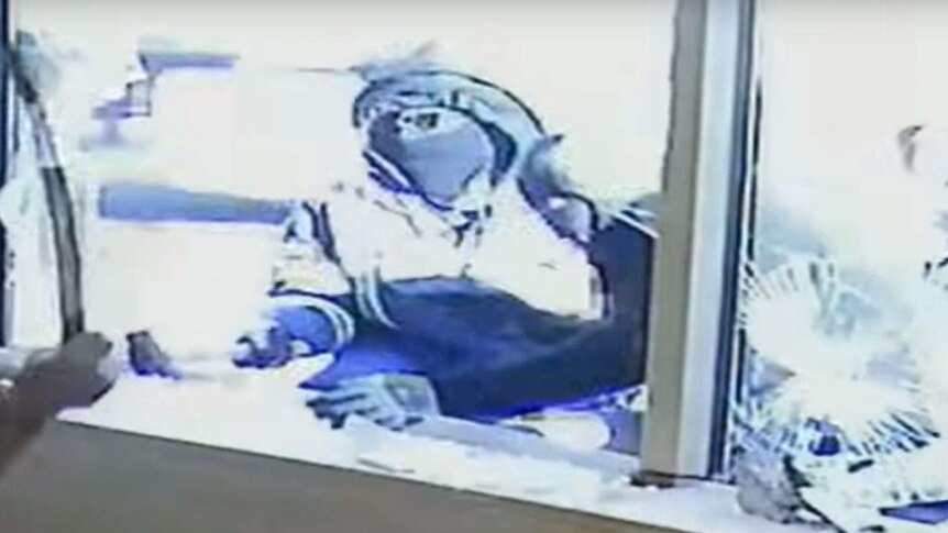 A blurry still from a CCTV footage of a man brandishing a sword through a broken window.