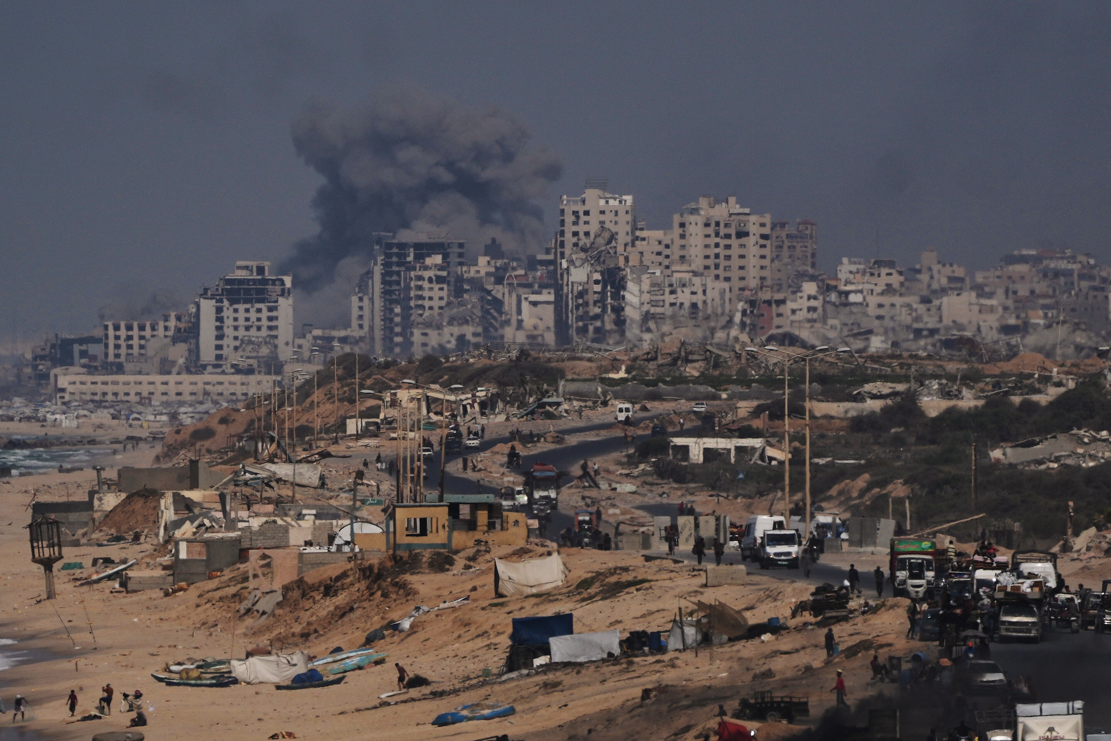 Smoke rising from a building in the distance standing among other buildings hit by military strikes.