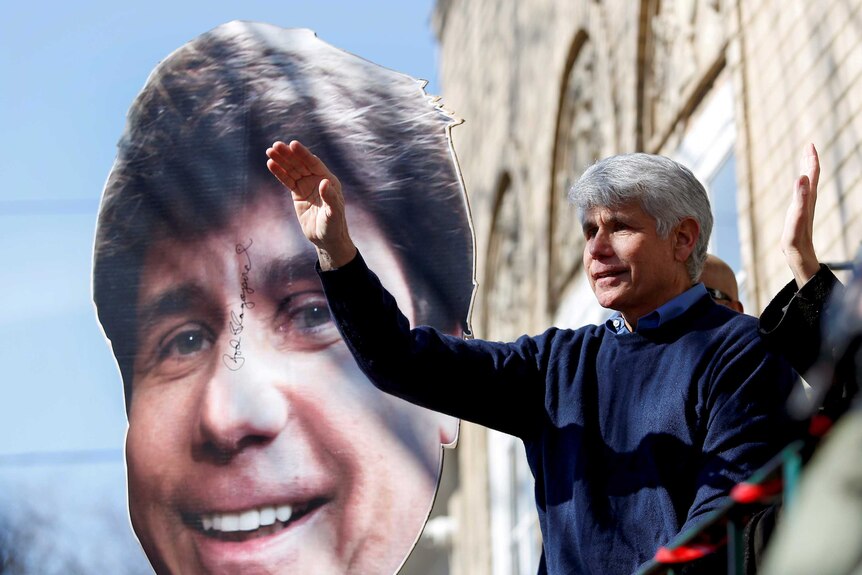 Rod Blagojevich waving to a crowd in front of a giant cut out of his face