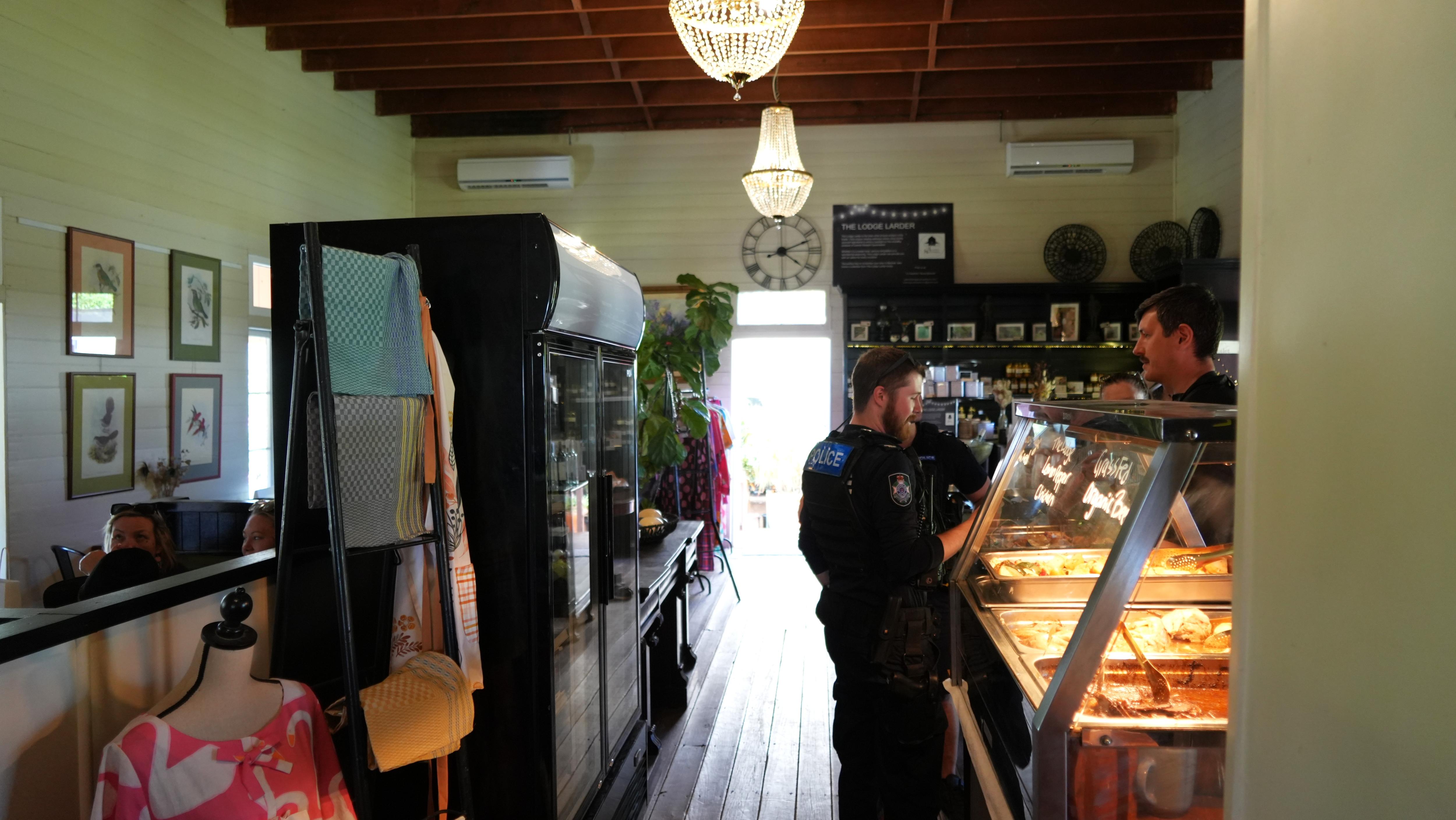Shop interior with chandeliers, a cafe counter, fridges and clothing for sale. Two men stand either side of the counter.