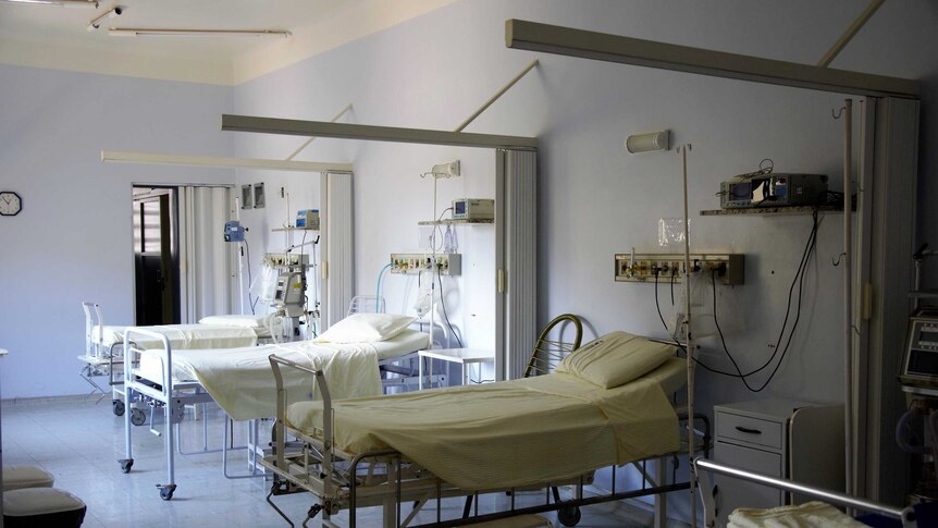 Three empty hospital beds in a ward