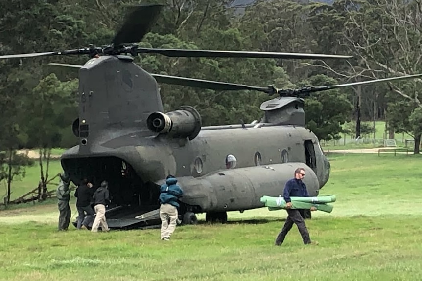 People walking around a greenish grey chinook helicopter on the ground