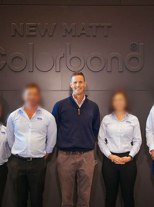 Jason Ellis stands at the centre of two women and three men, wearing business shirts in front of a Colorbond logo.
