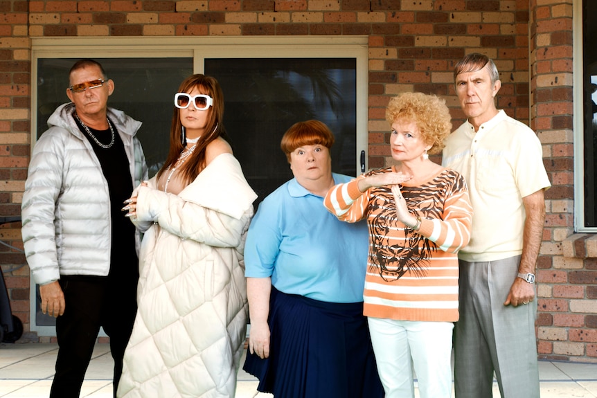 The cast of Kath and Kim pose in front of their brick house. 