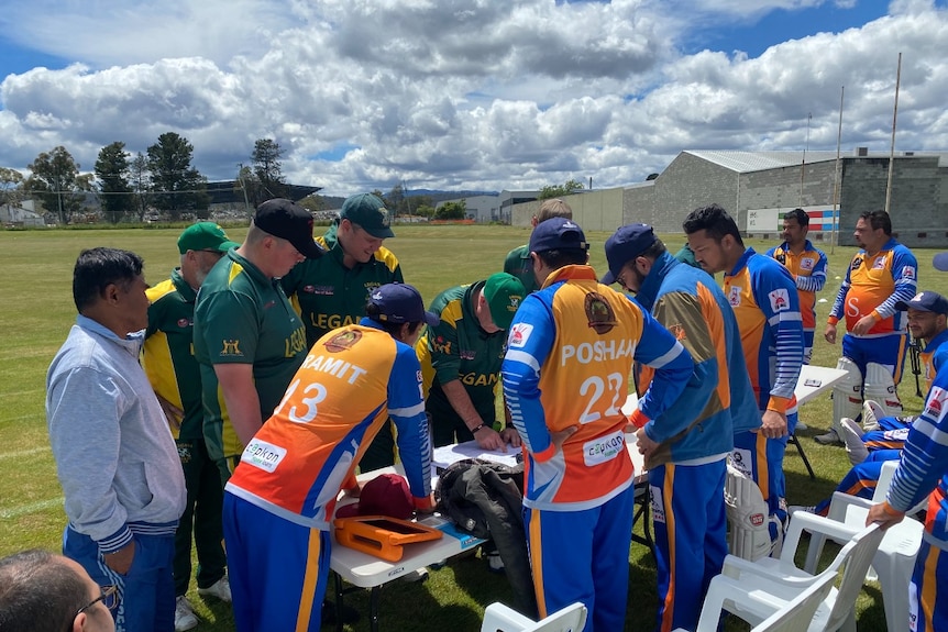 Members of a cricket team huddle over a table to discuss a game plan