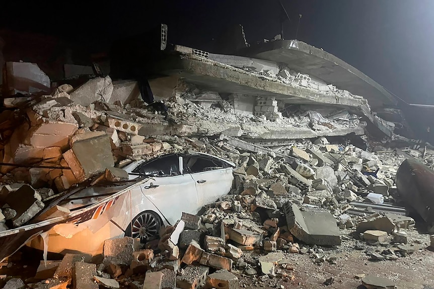 A car is seen under the wreckage of a collapsed building.