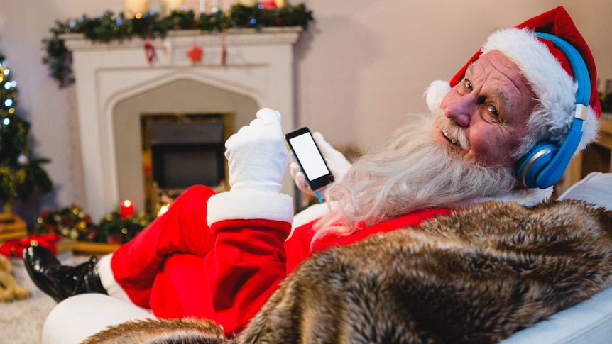 Father Christmas sitting with headphones on looking at his phone