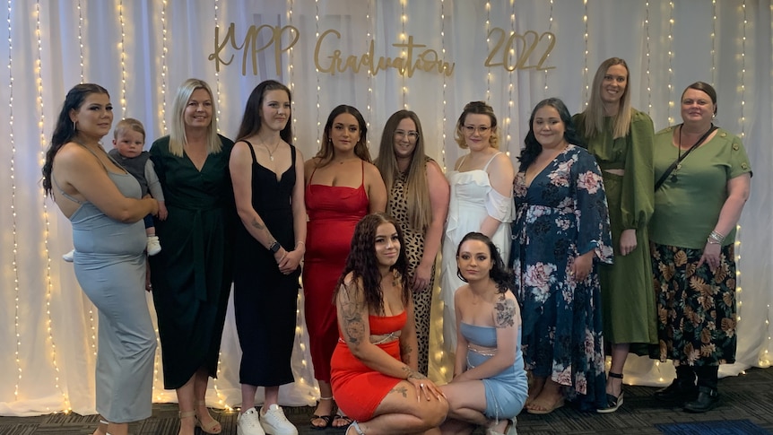 stage lineup of young mums in formal wear posing for photo   