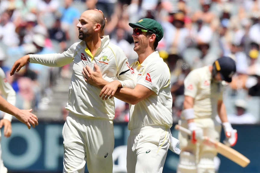 Nathan Lyon is congratulated by teammate Mitchell Marsh with a disappointed English batsman in the background