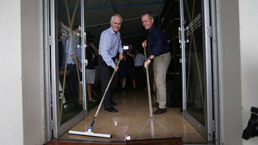 PM Turnbull and opposition leader Shorten sweep water out of a flood damaged shop.