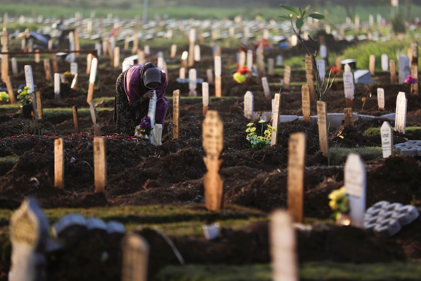 A woman wearing a purple shirt and hihab leans over a grave.