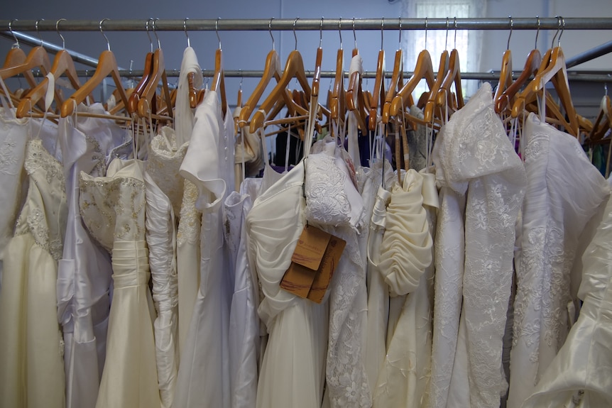 A rack of wedding dresses handing on coat hangers.