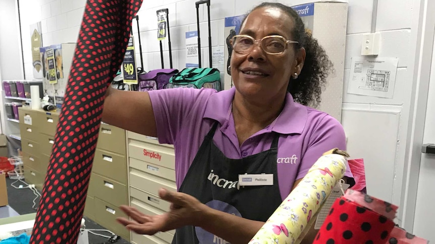 Woman of Torres Strait Islander appearance holding up a bolt of fabric in a Lincraft store