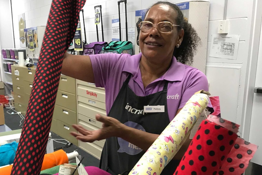 Woman of Torres Strait Islander appearance holding up a bolt of fabric in a Lincraft store