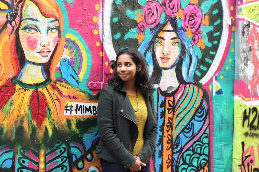 Remya Ramesh smile while standing in front of street art, for a story on career goals.