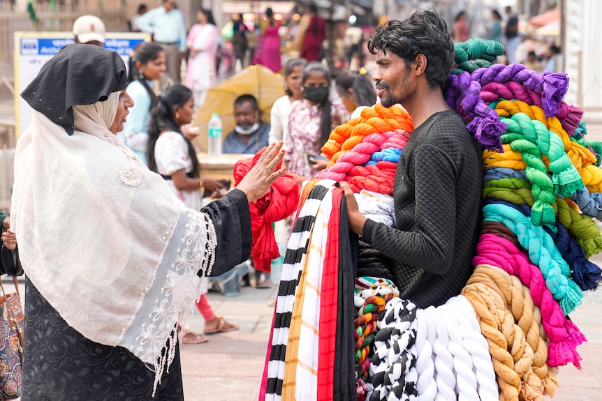 A man holds colourful clothes and is in discussion with a woman in a busy street