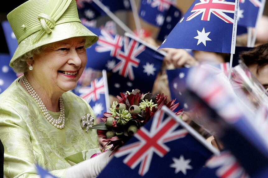 The queen smiles as holds a native bouquet amid a sea of Australian flags