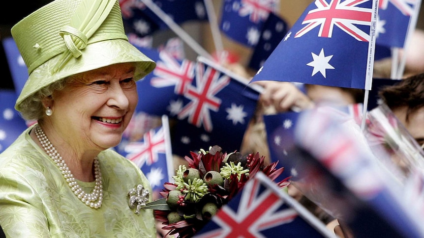 The queen smiles as holds a native bouquet amid a sea of Australian flags