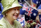 The queen smiles as holds a native bouquet amid a sea of Australian flags