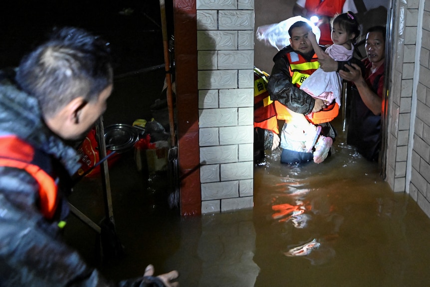 A rescue worker holds a small child through a flooded doorway