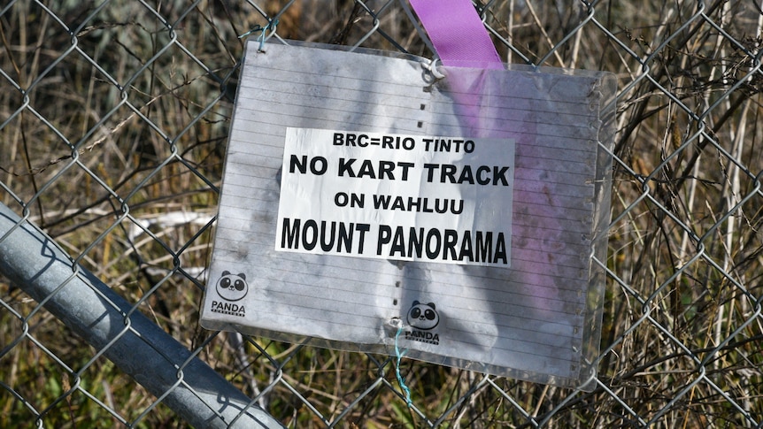 A paper sign tied to a chain link fence reads 'BRC=Rio Tinto - no kart track on Wahluu Mount Panorama'
