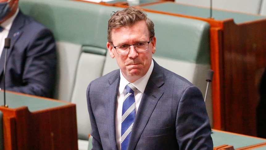 A man in a suit grimaces, with green seats in the background.