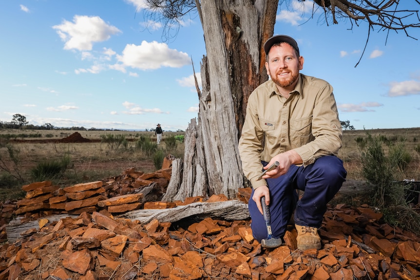 Dr Matthew McCurry kneeling on cracked red earth in front of tree