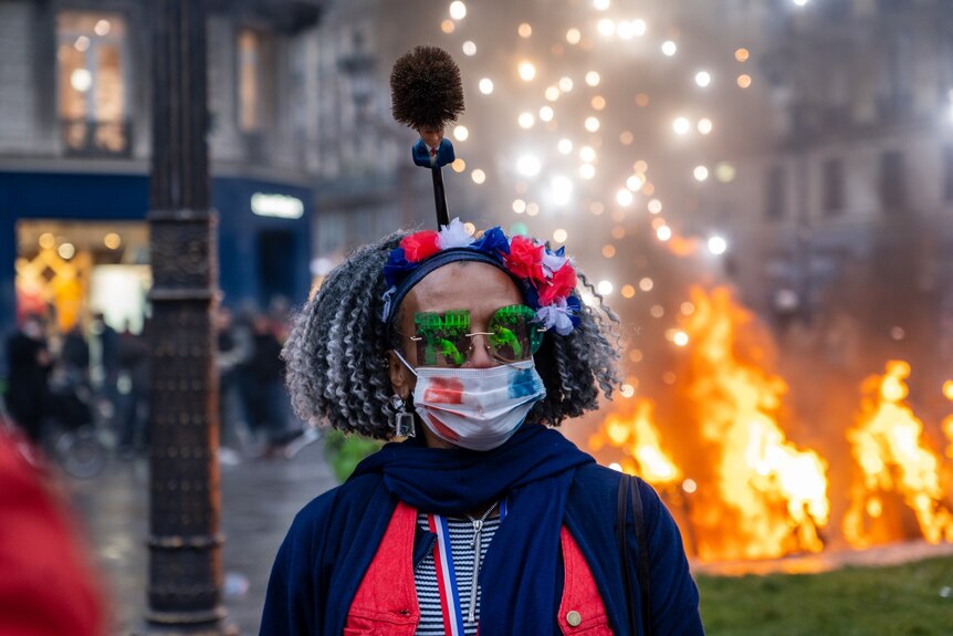 A woman wears glasses in the shape of 'No' and a face mask in the french flag colours.