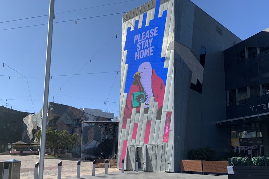 A sign reads 'Please Stay Home' with artwork of a seagull wrapped in a blanket holding a mug.