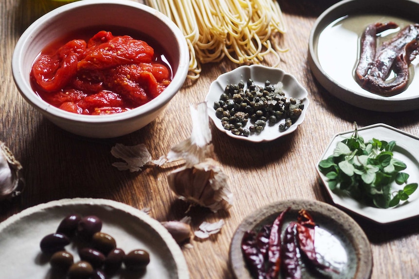 Ingredients for a spaghetti alla Puttanesca including tinned tomatoes, olives, capers, garlic, chilli, oregano, anchovies.
